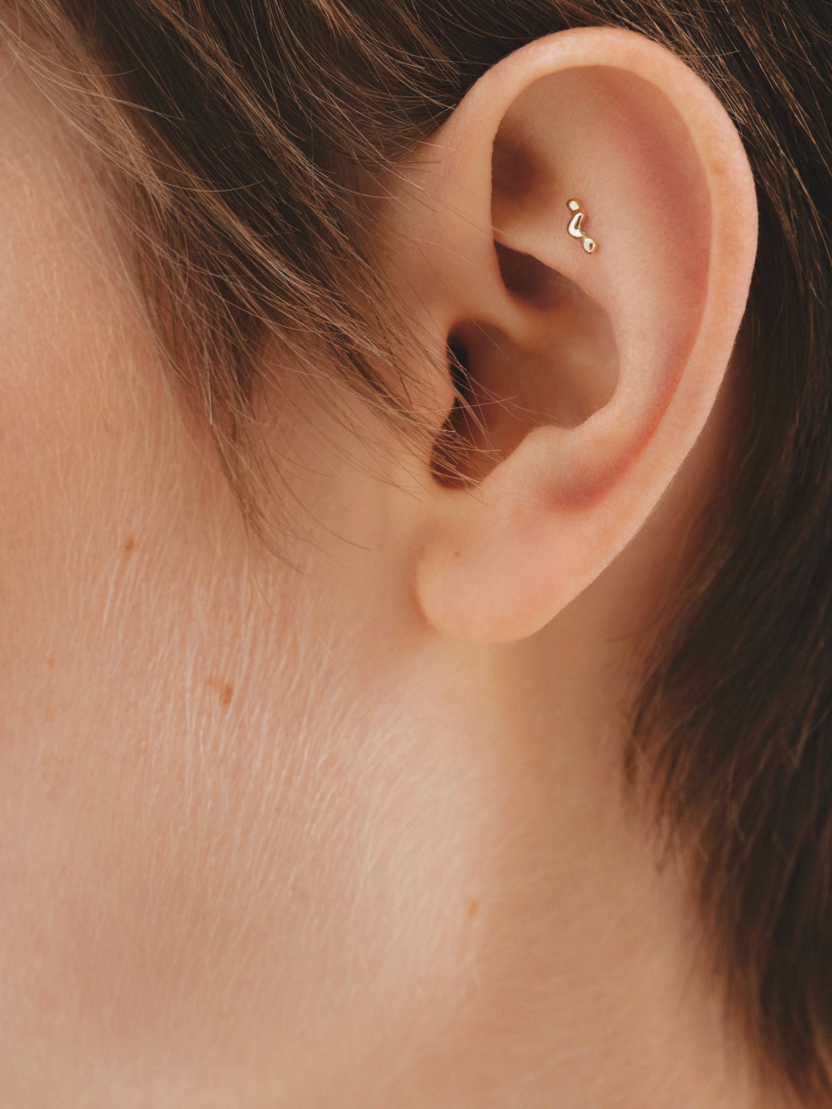 Individual 18K yellow gold piercing with an organic wave shape